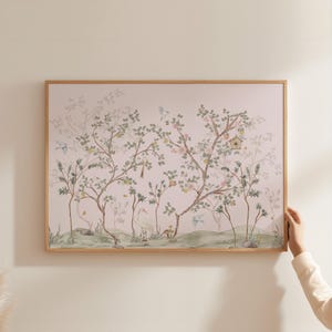 A person is holding up a framed painting of a tree with birds and flowers on a wall.