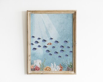 May include: Watercolor print of an underwater scene with a school of blue fish and one orange and white clownfish. The artwork is framed in a light brown wooden frame, with coral and plants at the bottom.