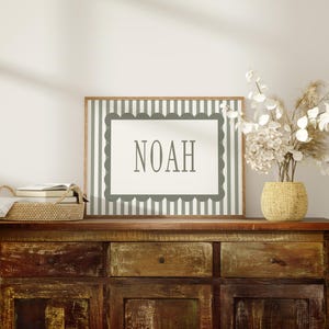 a wooden dresser with a framed sign that says "NOAH" on it, a woven basket, and a vase of white flowers.