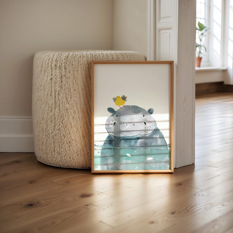 a framed picture of a hippopotamus with a yellow bird perched on its head, placed on a wooden floor next to a round white ottoman.