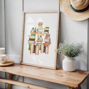 a wooden bench with a framed print of stacked books on top of it, placed on a shelf next to a vase with greenery.