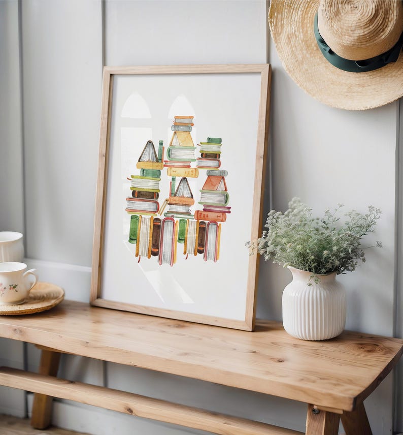 a wooden bench with a framed print of stacked books on top of it, placed on a shelf next to a vase with greenery.