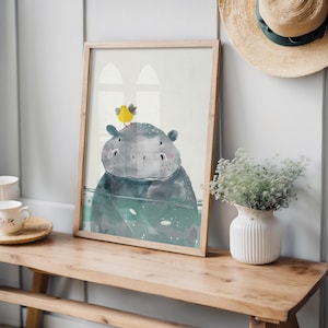 a wooden table with a framed picture of a hippopotamus and a yellow bird on top of it, along with a white vase with greenery and a straw hat on the wall.