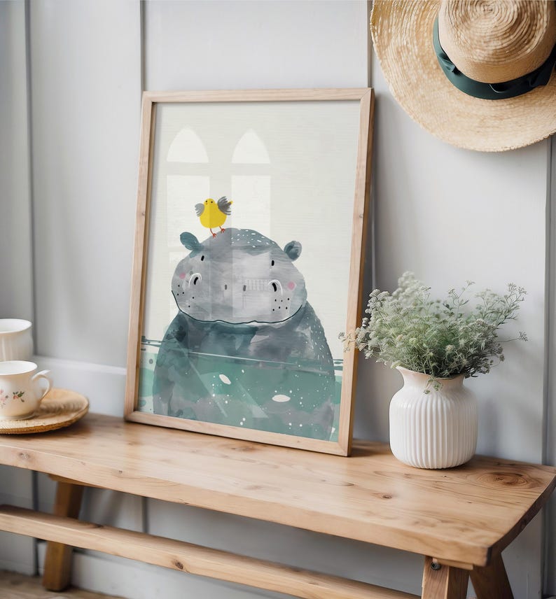 a wooden table with a framed picture of a hippopotamus and a yellow bird on top of it, along with a white vase with greenery and a straw hat on the wall.