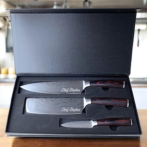 May include: A black box with a set of three kitchen knives with wooden handles. The knives are engraved with the text "Chef Stephen".