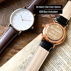 May include: Two wristwatches with leather bands. One has a brown band and a white face with gold-tone hands. The other watch has a black band and a rose gold case. The watch face says "My favorite time is with you."