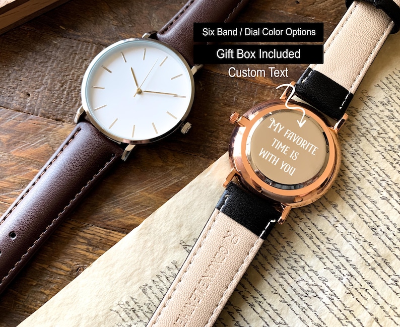 May include: Two wristwatches with leather bands. One has a brown band and a white face with gold-tone hands. The other watch has a black band and a rose gold case. The watch face says "My favorite time is with you."