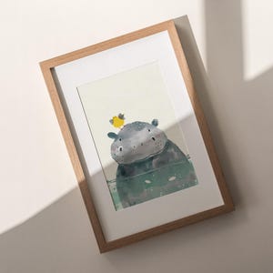 a framed artwork depicting a whimsical scene with a small, cartoonish creature, possibly a hippopotamus, sitting on a surface and looking up at the viewer.