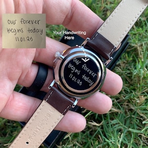 May include: A wristwatch with a brown leather strap and a silver-colored case. The watch face has the inscription "our forever begins today 11.01.25". The words "Your Handwriting Here" are also visible.