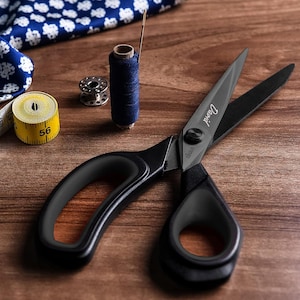 May include: Black fabric shears with a black handle and a silver screw. The shears have the word "Dritz" printed on the blade.