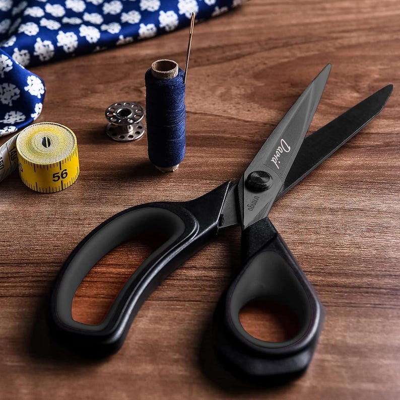 May include: Black fabric shears with a black handle and a silver screw. The shears have the word "Dritz" printed on the blade.