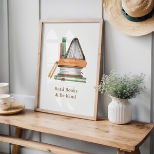 a wooden bench with a framed poster of a stack of books next to it, along with a vase of greenery and a straw hat on a shelf.