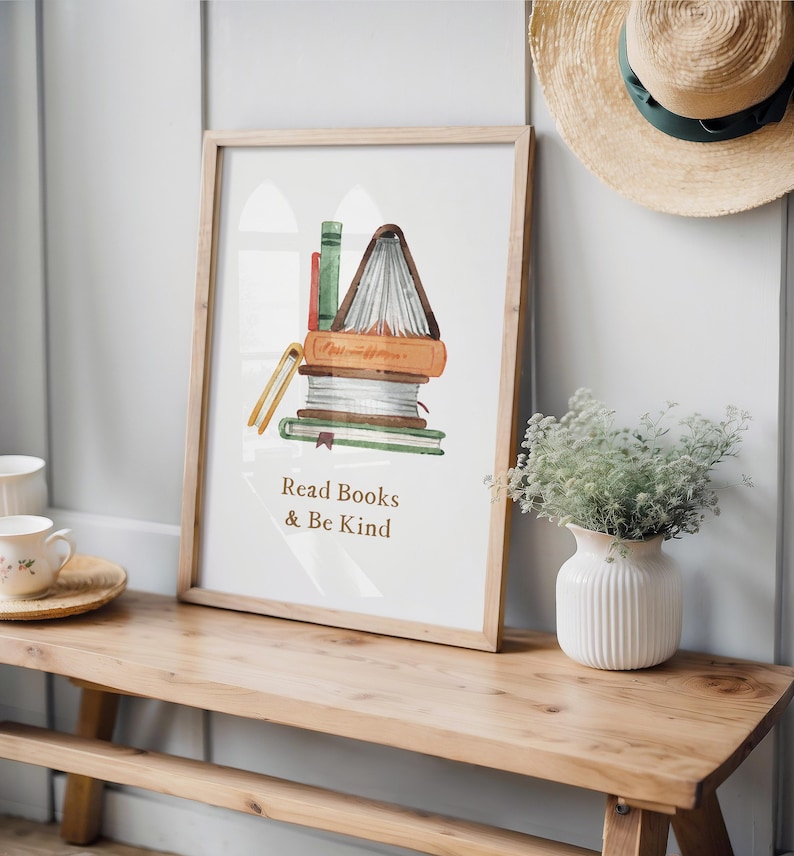 a wooden bench with a framed poster of a stack of books next to it, along with a vase of greenery and a straw hat on a shelf.