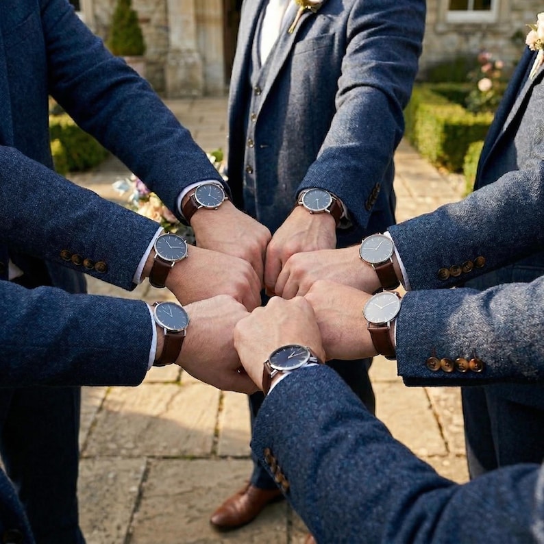 May include: A group of people wearing navy blue suits and brown leather strap watches with silver watch faces. The watches are the focal point, with the arms forming a circle.
