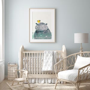 A nursery room with a wooden crib, a rocking chair, and a framed picture of a hippo on the wall.
