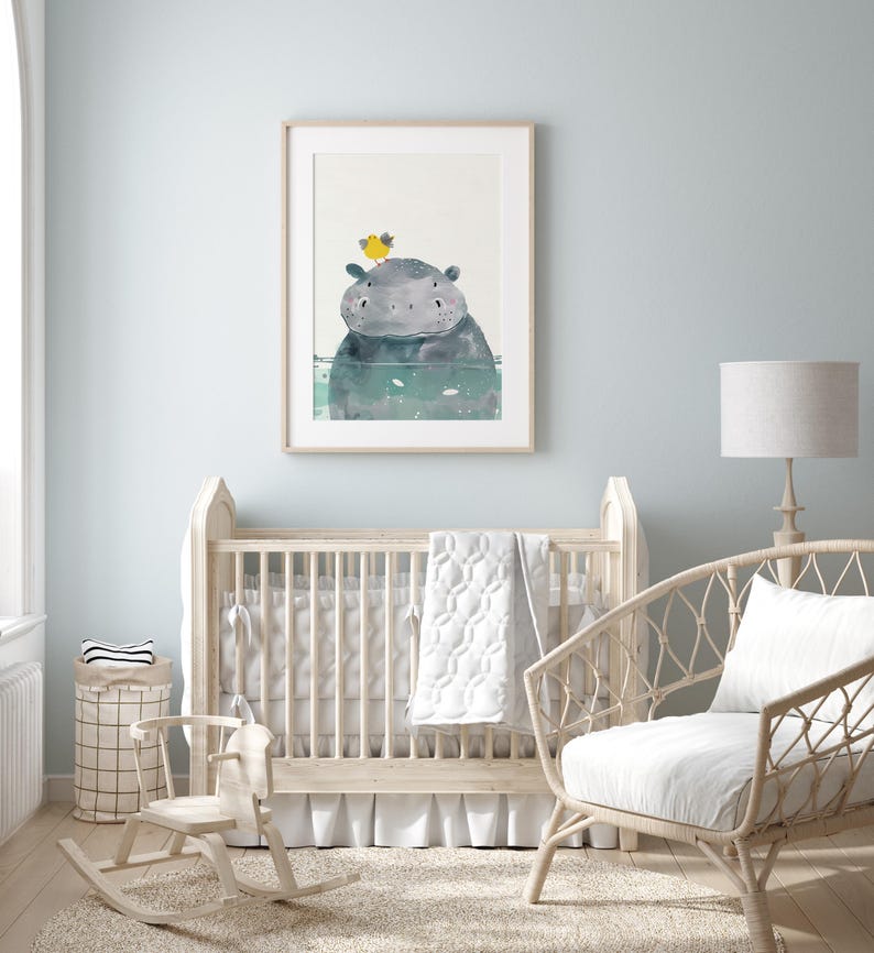 A nursery room with a wooden crib, a rocking chair, and a framed picture of a hippo on the wall.