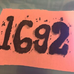 May include: A pink fabric patch with the number 1692 printed in black paint.