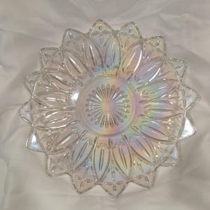 Peut inclure: Plat de service en verre transparent avec un motif de tournesol. Le plat présente une zone centrale circulaire avec un motif en étoile, entourée de bords en forme de pétales. Le verre a un éclat irisé, reflétant un arc-en-ciel de couleurs.