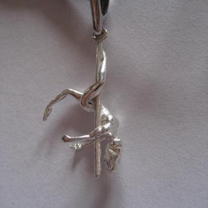 Può includere: Una collana con un ciondolo d'argento che rappresenta una persona appesa a testa in giù a un palo. Il ciondolo è attaccato a un cordino di cuoio nero.