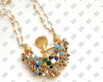 Puede incluir: Un collar de oro con un gran colgante con un diseño geométrico y colorido. El colgante está adornado con una variedad de piedras preciosas y un pequeño encanto de serpiente de oro. El collar está enhebrado con perlas blancas.