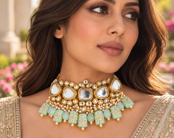 Puede incluir: Un collar tipo gargantilla en tono dorado con grandes piedras transparentes facetadas en monturas de metal ornamentadas, acentuado con pequeñas perlas blancas y cuentas rectangulares de color verde menta claro con motivos florales dorados.