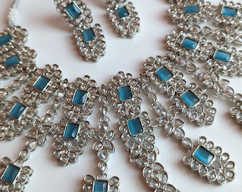 Puede incluir: Un conjunto de collar de plata con piedras azules y transparentes. El collar tiene un colgante con una piedra azul grande rodeada de piedras transparentes más pequeñas. Los pendientes también son de plata con piedras azules y transparentes.