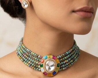Puede incluir: Un collar tipo gargantilla de varias hileras con pequeñas cuentas moteadas de color turquesa y un colgante circular central con una gran piedra clara en forma de pera rodeada de piedras rectangulares multicolores y pendientes a juego.