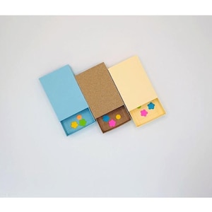 May include: Three rectangular boxes with open drawers, each in a different color: light blue, brown, and pale yellow. The drawers contain colorful, flower-shaped confetti. The boxes are arranged diagonally on a white surface.