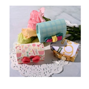 May include: Three small gift boxes with different patterned paper and ribbon bows. The boxes are on a white doily.