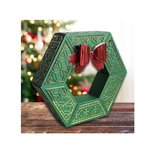 May include: A green hexagonal box with a gold geometric pattern and a red bow. The box is designed to look like a Christmas wreath.