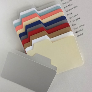 May include: A stack of ten different colored paper dividers with tabbed edges. The colors are silver gray, white, soft blue, salmon pink, ivory, navy blue, kraft gray, red, kraft brown, white, and cream.