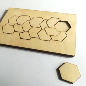 Könnte beinhalten: Ein Holzpuzzle mit einem fehlenden Teil. Das Puzzle besteht aus sechseckigen Formen und ist zum Zusammensetzen gedacht. Das fehlende Teil ist ein separates Sechseck.