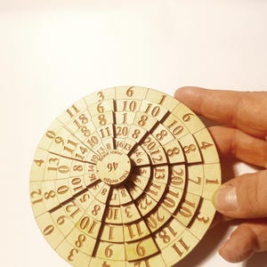 May include: A circular wooden puzzle with concentric rings of numbers. The puzzle is a brain teaser with the text "Brain Teaser" and "Prata me" printed on it.