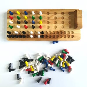 May include: A wooden game board with a grid of holes and a separate compartment for storing game pieces. The game pieces are colorful and include black, white, red, yellow, green, and blue. The game board is made of light wood and has a natural finish.