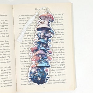 May include: A colourful bookmark featuring a stack of mushrooms with red, pink, and blue caps. The mushrooms are surrounded by green leaves and flowers. The bookmark has a white tassel.