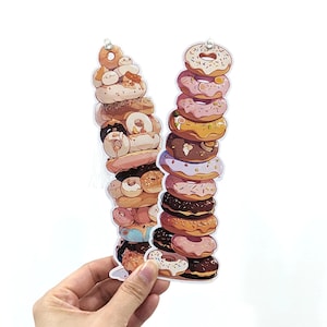 May include: Two stacks of colorful donuts, one with a variety of glazes and sprinkles, the other with pink, white, and brown frosting. The donuts are stacked on top of each other, creating a tall tower.