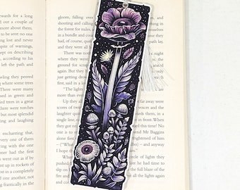 May include: A purple and black bookmark with a large purple flower, mushrooms, and other foliage. The bookmark has a tassel on the bottom.
