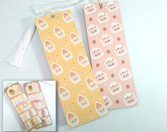 May include: Two colorful bookmarks with cute patterns. One bookmark features a yellow background with a repeating pattern of pink cupcakes with happy faces. The other bookmark has a pink background with a repeating pattern of pink cakes with happy faces and strawberries. Both bookmarks have white tassels.