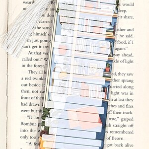 Pode incluir: Um marcador de p&aacute;gina colorido com um design de estante. O marcador &eacute; feito de papel e tem uma borla branca. A estante est&aacute; cheia de livros e plantas. O texto no marcador diz "died of", "wly and", "would", "sleep."