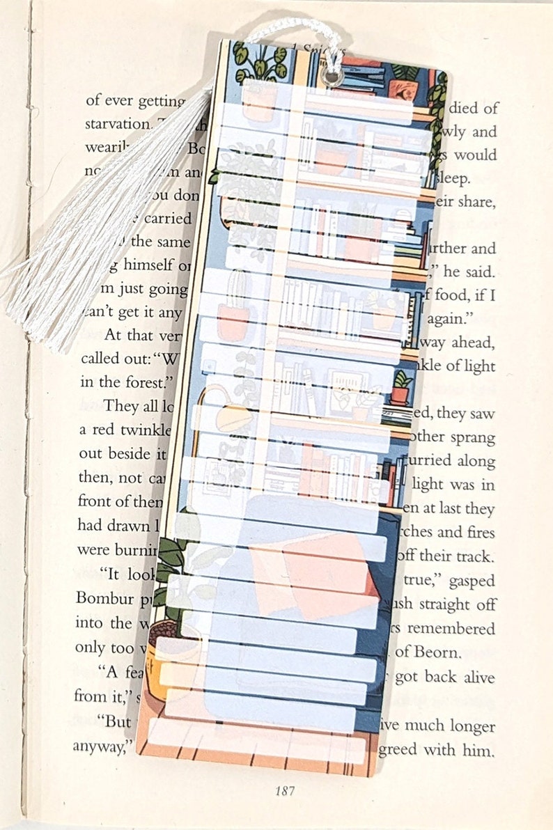 Pode incluir: Um marcador de p&aacute;gina colorido com um design de estante. O marcador &eacute; feito de papel e tem uma borla branca. A estante est&aacute; cheia de livros e plantas. O texto no marcador diz "died of", "wly and", "would", "sleep."