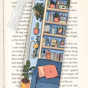 Pode incluir: Um marcador de p&aacute;gina com uma ilustra&ccedil;&atilde;o colorida de uma estante com livros, plantas e uma poltrona aconchegante. O marcador &eacute; feito de acr&iacute;lico transparente e tem uma borla branca.
