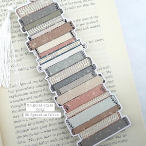 Puede incluir: Una pila de 30 lomos de libros en varios tonos de gris, azul, rosa y marr&oacute;n. Las lomos est&aacute;n decoradas con dise&ntilde;os florales y un aspecto desgastado y vintage. El marcap&aacute;ginas est&aacute; etiquetado como "Estilo original: Acogedor" y "30 lomos para rellenar".