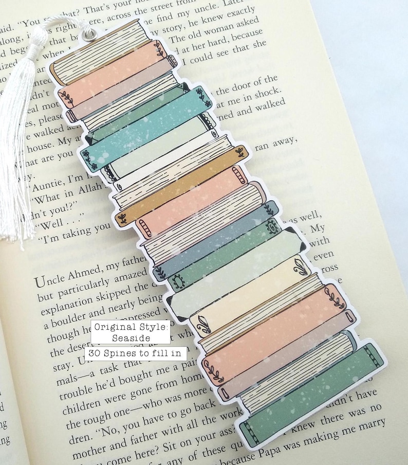 Puede incluir: Una pila de 30 lomos de libros con un tema costero de ensue&ntilde;o. Las lomos est&aacute;n ilustradas con una variedad de colores y patrones, incluyendo azul, verde, rosa y blanco. El texto "Original Style Seaside" y "30 Spines to fill in" es visible en el marcap&aacute;ginas.