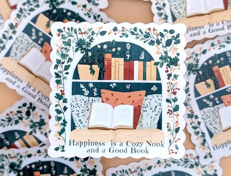 Puede incluir: Una pegatina que representa una escena de rinc&oacute;n de lectura. La ilustraci&oacute;n muestra una ventana con una estanter&iacute;a, un libro abierto y cojines. El follaje verde enmarca la escena, y el texto "Happiness is a Cozy Nook and a Good Book" est&aacute; en la parte inferior.