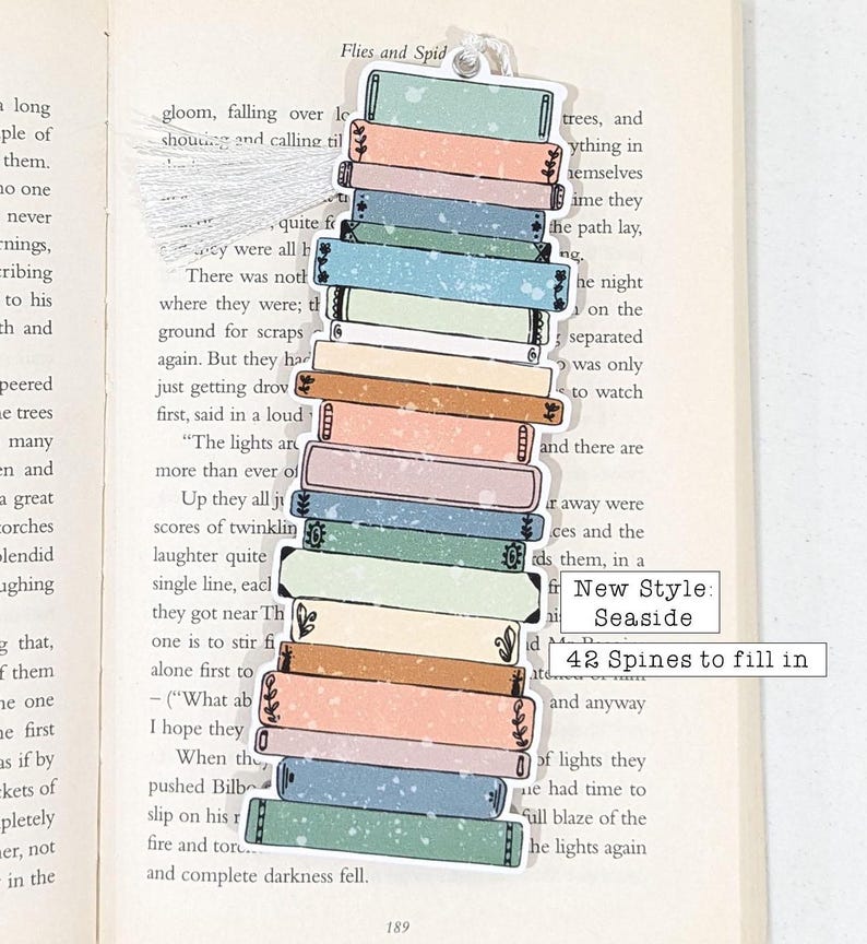 Puede incluir: Una pila de 14 lomos de libros coloridos con un marcap&aacute;ginas de borla blanca. El marcap&aacute;ginas tiene el texto "New Style: Seaside 42 Spines to fill in".