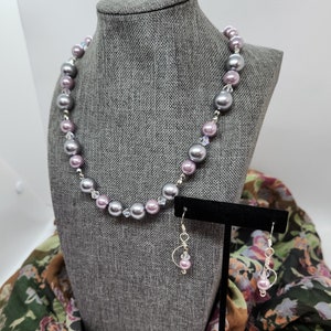 May include: A gray and purple pearl necklace with crystal accents, matching earrings, and a floral patterned scarf.