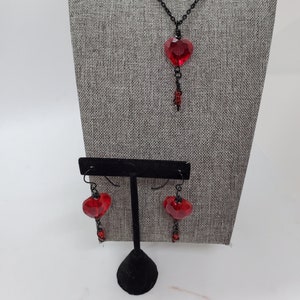 May include: A red heart-shaped crystal pendant necklace and matching earrings with black chain and wire accents.