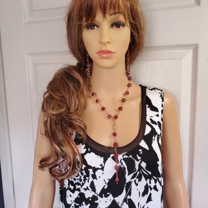 May include: A long, dangling necklace and matching earrings with maroon beads and gold chain accents.