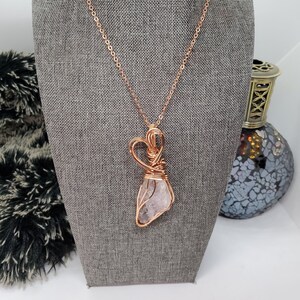 May include: A rose gold necklace with a clear quartz crystal wrapped in wire and a heart-shaped wire design.