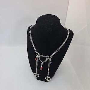 May include: A silver-toned necklace with a heart-shaped pendant and dangling heart charms. The necklace features a chain design and is adorned with red and purple beads. The WiredLoop@etsy.com is printed at the bottom.